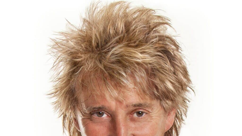 Rod Stewart performing on stage at a concert with vibrant lights and an engaged audience.