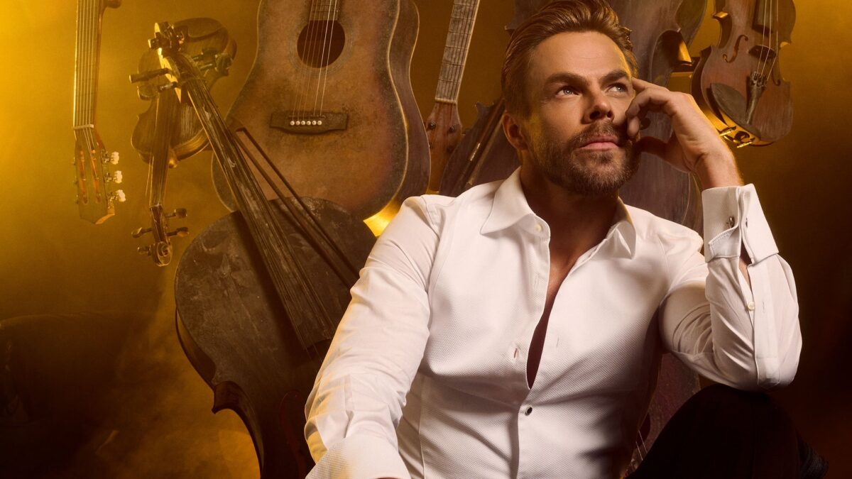 Derek Hough performing on stage at The Midland Theatre, surrounded by vibrant lights and an engaging audience.